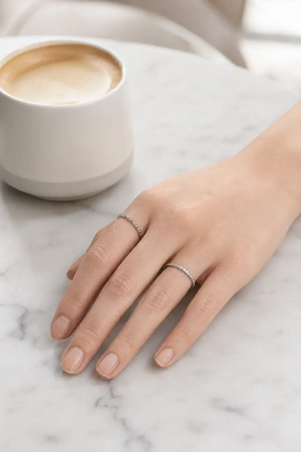 Slim diamond rings stacked on a hand at a cafe table