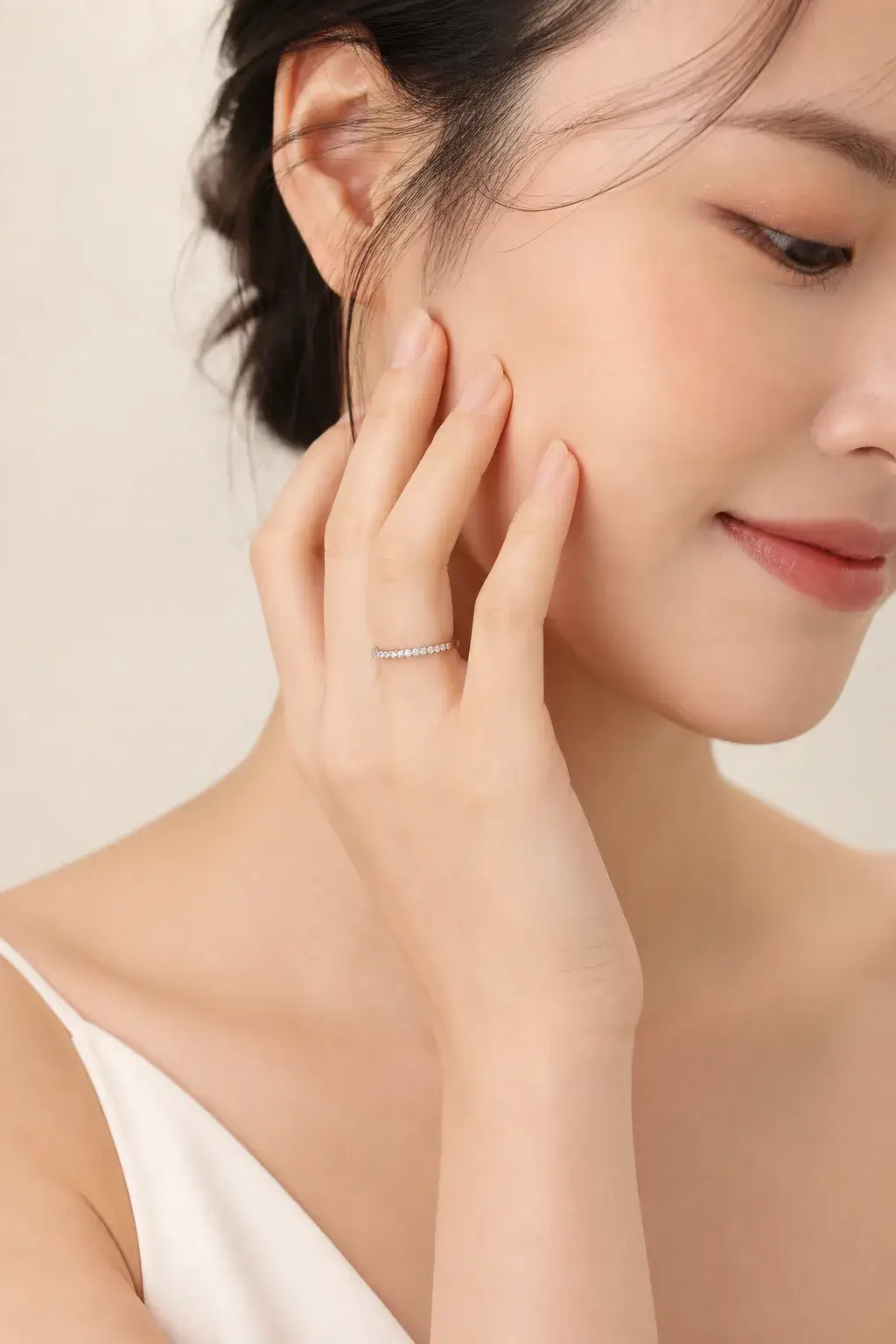 A slim white gold natural diamond eternity band worn on a hand resting near the cheek